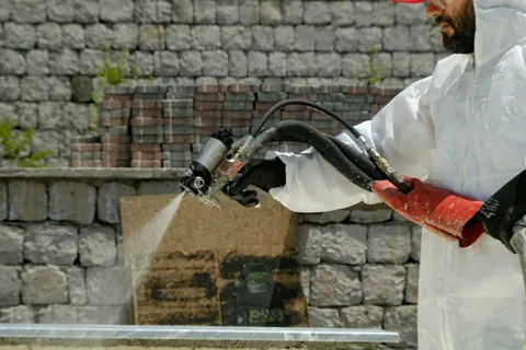 Technician in coveralls spraying a treatment on an exterior wall