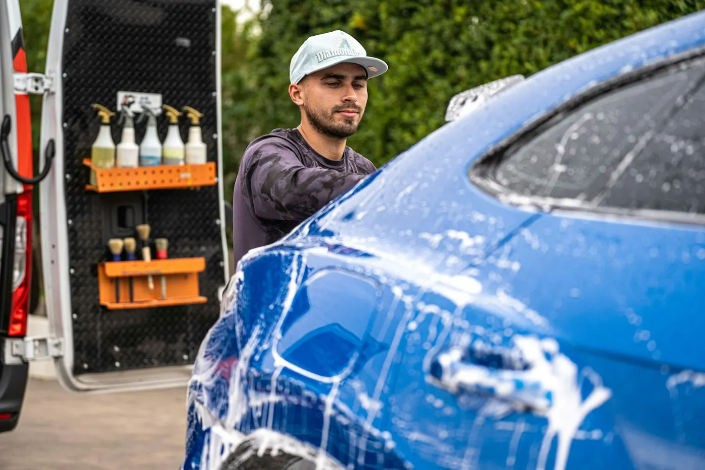 A mobile detailer washing a car with soap and foam